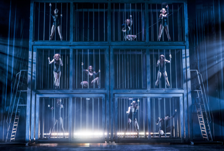 Scenbild från musikalen Chicago. Tre rader på höjden med burar. 12 stycken och i nio av dem står det dansare.