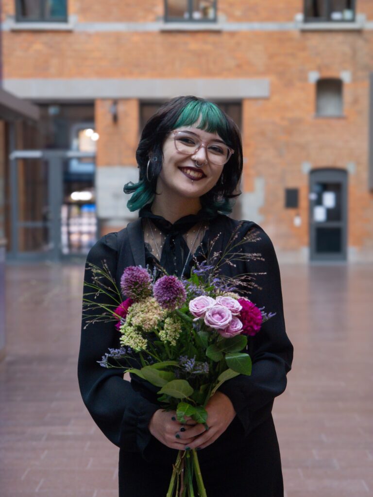 Max Sjöquist står framför en tegelbyggnad med en blombukett i händerna.