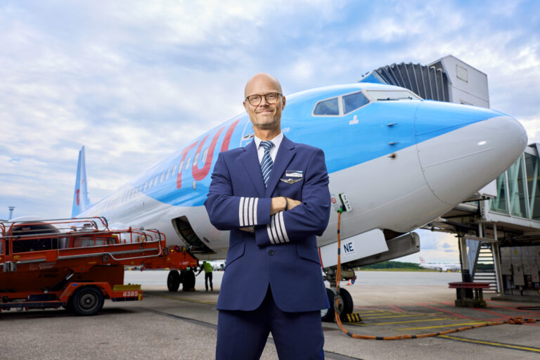 Markus står i flygkaptenskostym med armarna i kors utanför planet