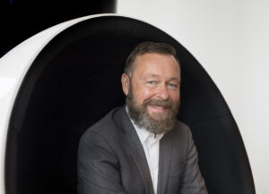 Man, Berndt Arell, i kostym sitter i modern stol och ler